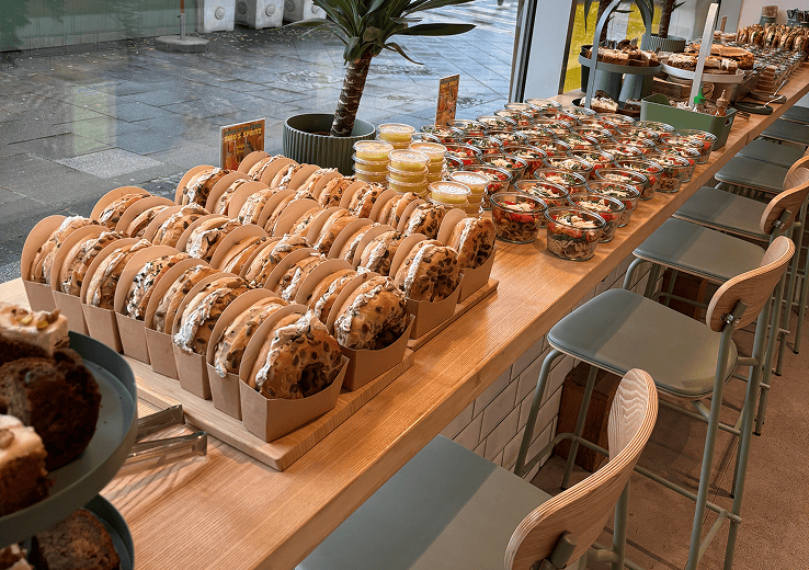 Ein Tisch voller Köstlichkeiten: Sandwiches, Desserts in Gläsern und Muffins in einer einladenden Caféteria.