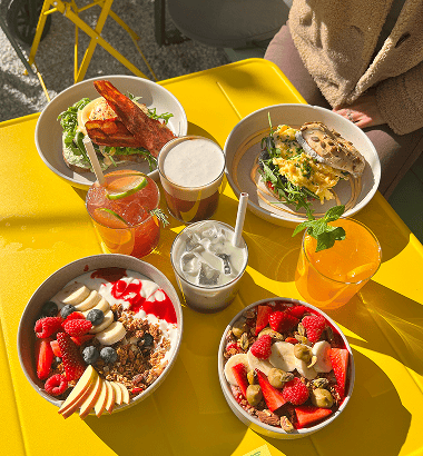 Ein buntes Frühstücksbuffet mit verschiedenen Gerichten und Getränken auf einem gelben Tisch.