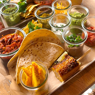 Ein Teller mit Tortillas, verschiedenen Salsas, frischem Gemüse und gegrilltem Mais.