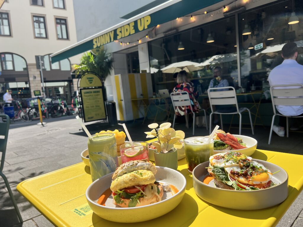 Bunt gedeckter Tisch mit verschiedenen Gerichten und Getränken vor einem Café namens "Sunny Side Up".