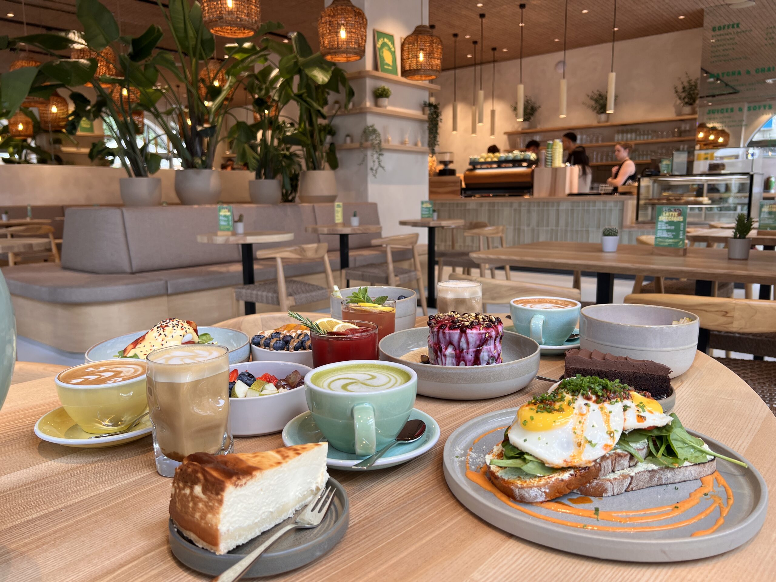 Bunt angerichtetes Frühstück mit Kaffee, Kuchen, Obst und einem Gericht mit Spinat und Spiegelei in einem stilvollen Café.