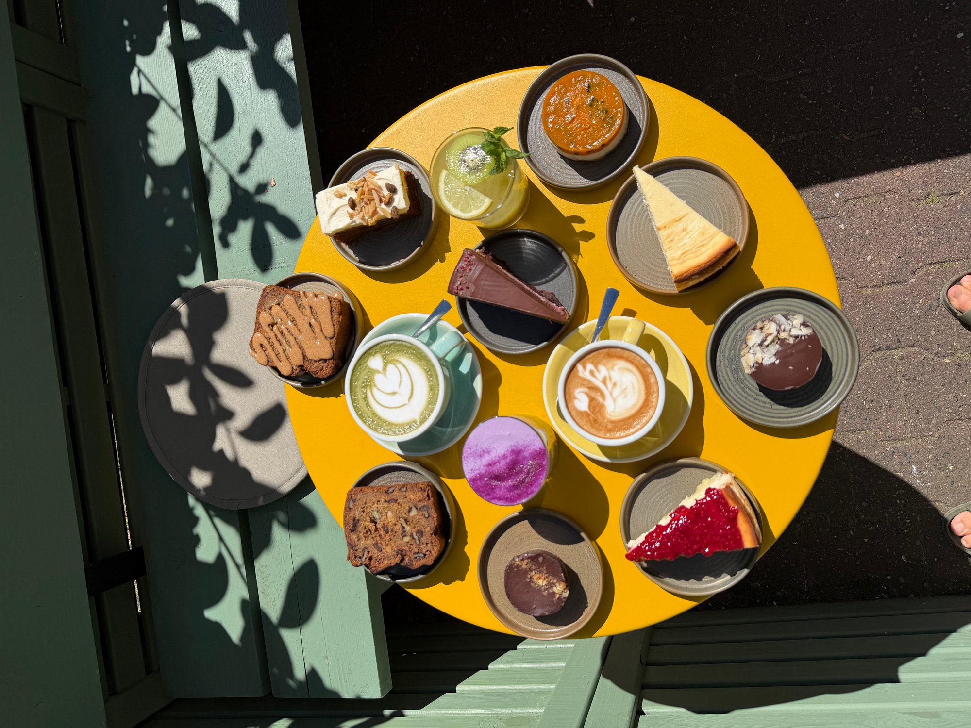 Verschiedene hausgemachte Kuchen, Tarte und Kaffee auf einem gelben Tisch im Sunny Side Up
