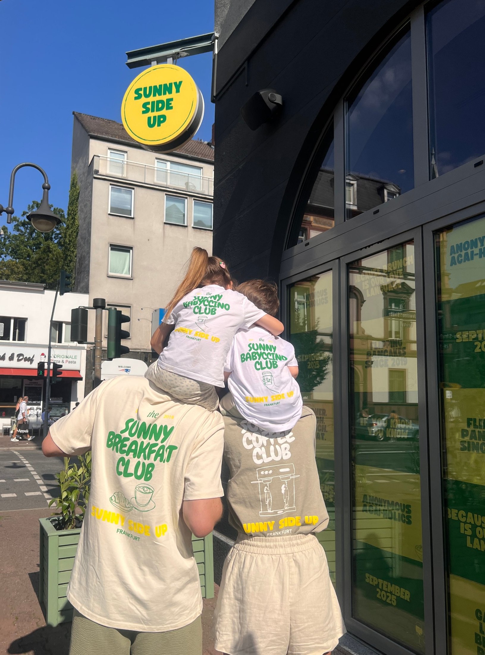 Zwei Kinder auf den Schultern ihrer Eltern vor dem Sunny Side Up